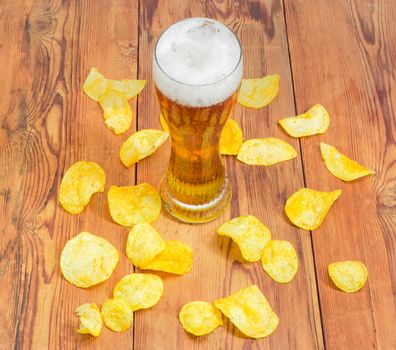 Top view of beer glassware with the lager beer among the potato chips scattered the old darkened by time wooden planks
