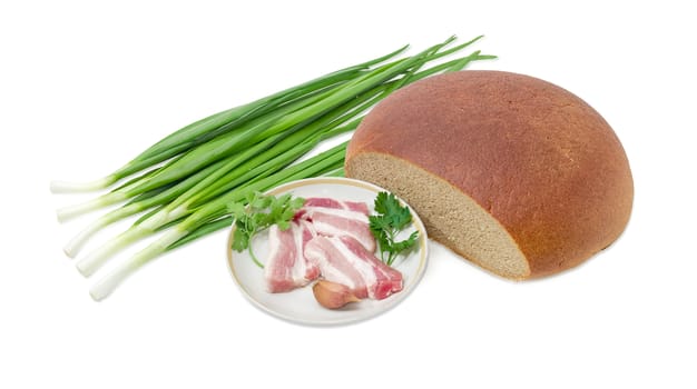 Several slices of uncooked streaky pork belly bacon, garlic, twigs of parsley and cilantro on dish,  partly incised hearth wheat and rye bread,  stalks of green onion on a light background 
