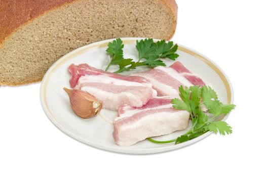 Several slices of uncooked streaky pork belly bacon, garlic, twigs of parsley and cilantro on saucer against the background of cut hearth brown bread closeup on a light background 
