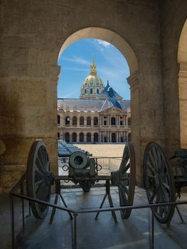 View through the arch to the Honorific Courtyard and a northern facade of the Saint Louis Des Invalides Church with the bronze cannons in the foreground in Paris
