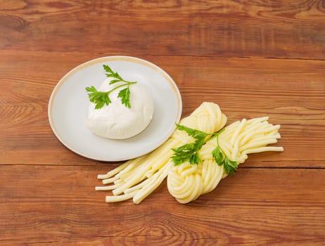 Ball of the fresh mozzarella cheese on the saucer, two portion of the mozzarella cheese in the shape of strings, twisted to form a plait and twigs of parsley on an old wooden surface
