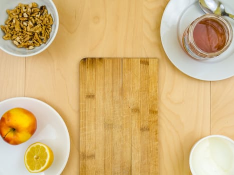 Four ingredients for a healthy and nutritious snack or smoothie, apple lemon fruit, cottage cheese, honey , shelled nuts walnuts, on plates from top view, arranged on wooden table in soft colours with copy space board in the middle