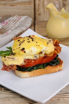 Eggs Benedict with tomato, slices of bacon, spinach under hollandaise sauce on toast