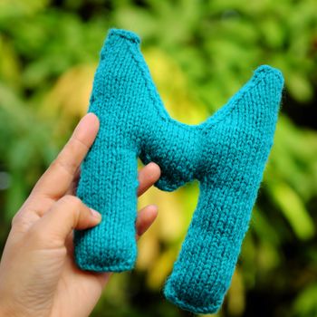 Woman hand pick knitted alphabet on green nature background, color handmade product knit from yarn with creative 