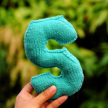 Woman hand pick knitted alphabet on green nature background, color handmade product knit from yarn with creative 