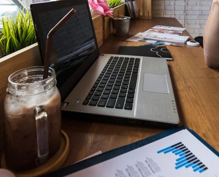 Coffee cup  on a table with laptob and graph finance diagram in coffee shop.