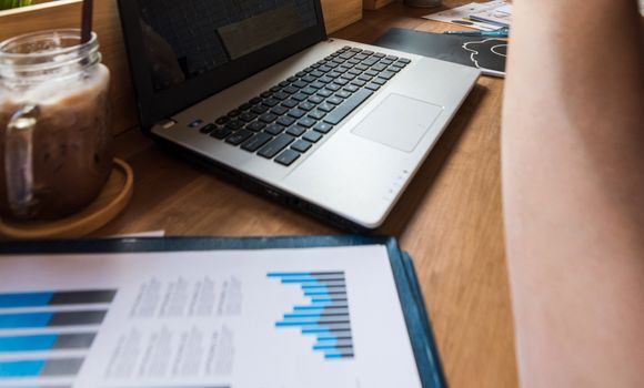 Coffee cup  on a table with laptob and graph finance diagram in coffee shop.