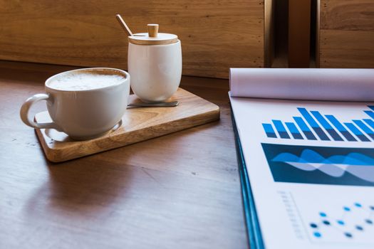 Coffee cup  on a table with laptob and graph finance diagram in coffee shop.