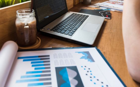 Coffee cup  on a table with laptob and graph finance diagram in coffee shop.