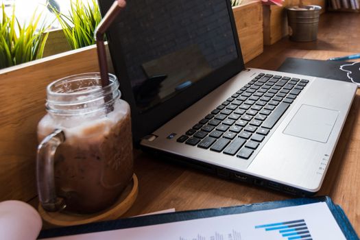 Coffee cup  on a table with laptob and graph finance diagram in coffee shop.