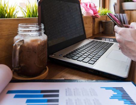 Coffee cup  on a table with laptob and graph finance diagram in coffee shop.