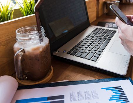 Coffee cup  on a table with laptob and graph finance diagram in coffee shop.