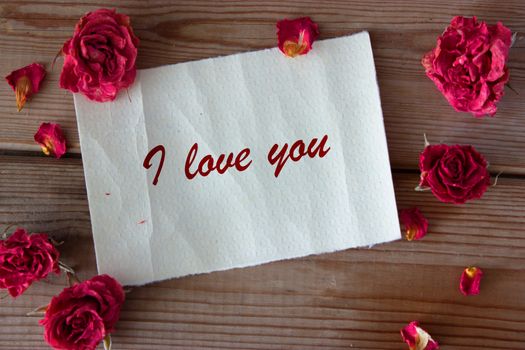 note and dry pink roses on wooden table