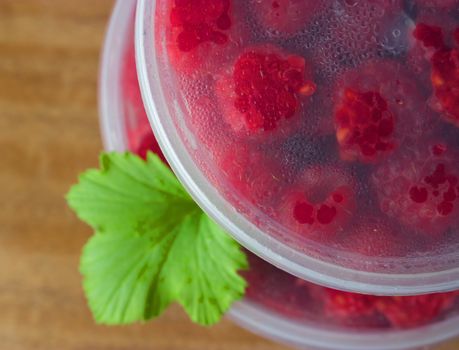 Raspberry in the round box with leaf of mint on the old wood background