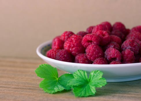 Ripe fresh raspberry in plate. wooden background