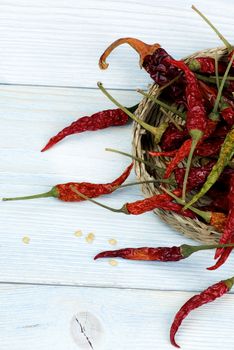 Arrangement of Dried Chili Peppers Full Body with Stems in Wicker Bowl closeup on Blue Wooden background. Top View