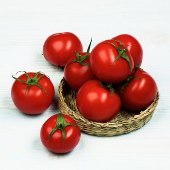 Arrangement of Ripe Raw Red Tomatoes with Stems in Wicker Plate closeup on Light Wooden background