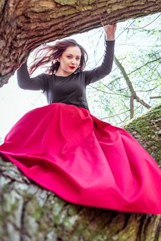 beautiful young woman in a red skirt sitting on a tree trunk in spring forest