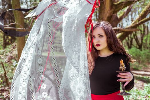 mysterious woman witch in the forest with a candle hidden behind the curtains