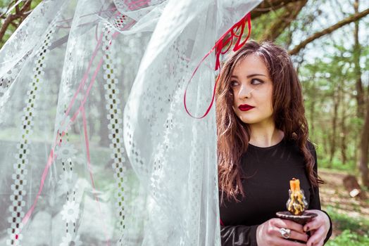 mysterious woman witch in the forest with a candle hidden behind the curtains