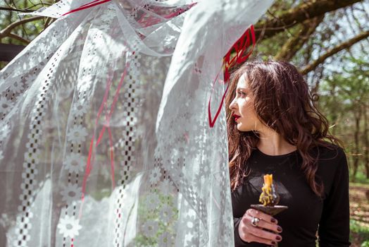 mysterious woman witch in the woods with a candle hidden behind the curtains