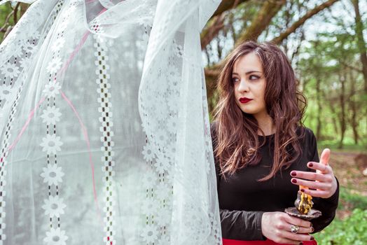 mysterious woman witch in the woods with a candle hidden behind the curtains