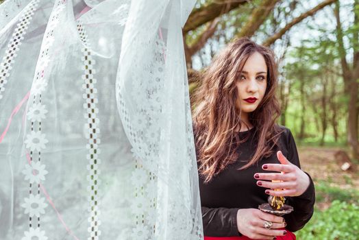 mysterious woman witch in the forest with a candle hidden behind the curtains