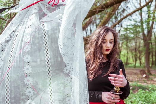 mysterious woman witch in the forest with a candle hidden behind the curtains