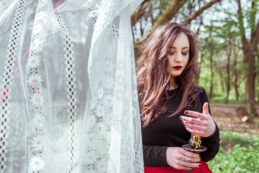 mysterious woman witch in the woods with a candle hidden behind the curtains