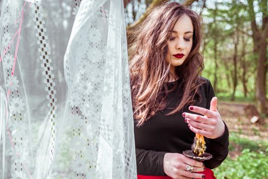 mysterious woman witch in the woods with a candle hidden behind the curtains