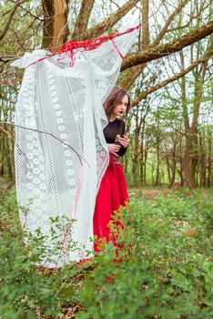 mystical witch woman in a red skirt with a candle hidden behind the curtains in spring forest