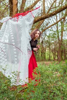 mystical witch woman in a red skirt with a candle hidden behind the curtains in spring forest