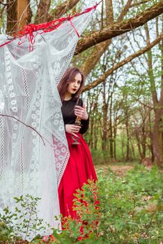 mystical witch woman in a red skirt with a candle hidden behind the curtains in spring forest