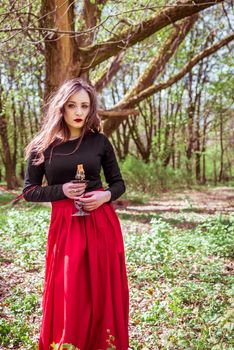 mystical witch woman in a red skirt with a candle in spring forest