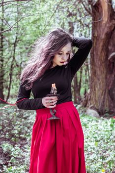 mystical witch woman in a red skirt with a candle in spring forest