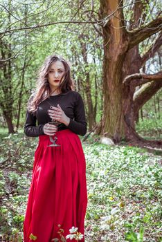 mystical witch woman in a red skirt with a candle in spring forest