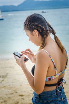 Beautiful young woman uses a smartphone on the beach. Filter vintage