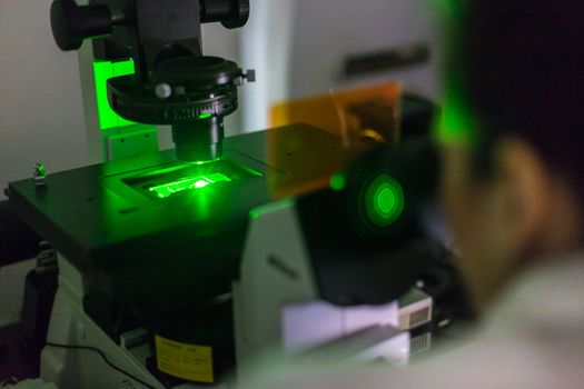 Life science female researcher microscoping with hi-tech fluorescent microscope in scientific genetic laboratory. Healthcare and biotechnology.