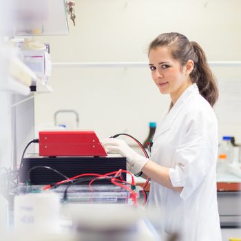 Focused attractive young life science researcher setting voltege on power supply to run electrophoresis for protein or DNA sepparation. Focus on the researcher's face.