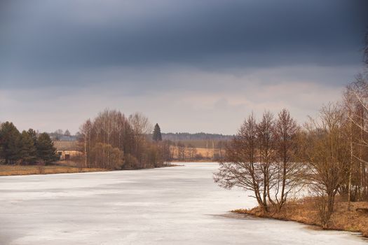 Spring rural scene. Lake under ice and snow melting. Cloudy spring day. Early spring. Mud season.