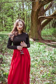 mystical witch woman in a red skirt with a candle in spring forest