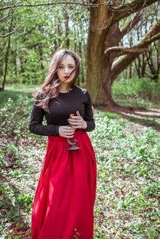 mystical witch woman in a red skirt with a candle in spring forest