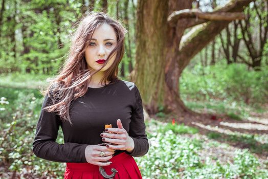 mystical witch woman in a red skirt with a candle in spring forest