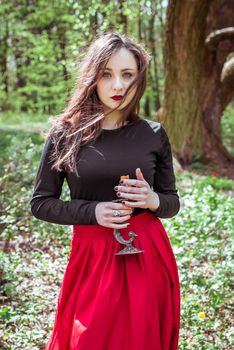 mystical witch woman in a red skirt with a candle in spring forest