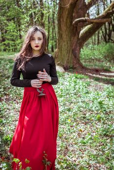 mystical witch woman in a red skirt with a candle in spring forest