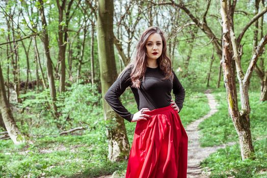 beautiful woman in a red dress standing in the spring forest