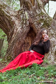 mystical witch woman sitting under a old tree in the spring forest