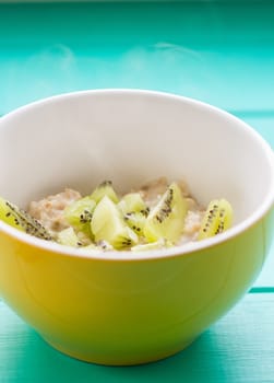 Oatmeal with milk and kiwi in a yellow bowl on a blue wooden table