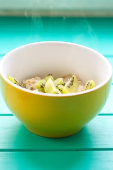 Oatmeal with milk and kiwi in a yellow bowl on a blue wooden table