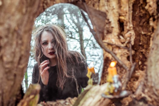 mystical woman looks in the mirror near a tree at the spring forest